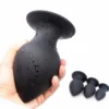 Mão segurando o butt plug anal grande de silicone preto ao lado dos tamanhos menores