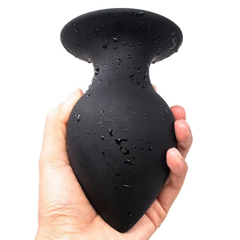 Plug anal grosso de silicone preto apoiado na mão, com a base em ventosa voltada para cima