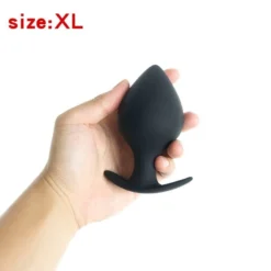 Mão segurando o plug anal de silicone preto em formato de pêssego, tamanho XL