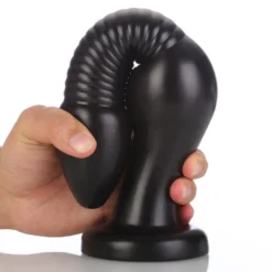 Plug anal enorme preto dobrado ao meio na mão, apoiado na ventosa