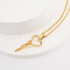 Colar com chave de castidade em formato de coração dourado apoiado em suporte claro