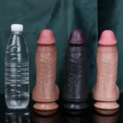 Dildos realísticos nas cores pele e preto ao lado de uma garrafa