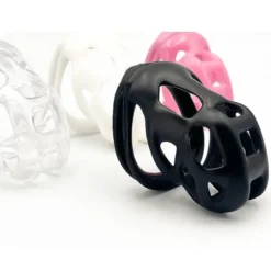 Gaiola de castidade masculina preta em primeiro plano com as versões rosa, branca e transparente ao fundo