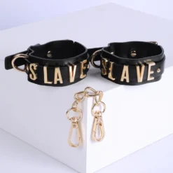 Par de algemas de couro preto com letras SLAVE e mosquetões dourados