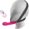 Vibrador rosa com arnês de queixo preso à cabeça por cintas elásticas, ao lado do controle remoto