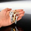 Mão segurando o colar chave de castidade de coração dourado, o de strass e as chaves do miolo