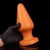 Plug anal gigante em cone de silicone líquido dourado segurado por mão de luva preta