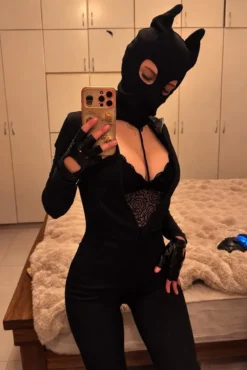 Mulher usando balaclava com chifres de demônio, macacão preto e luvas de couro